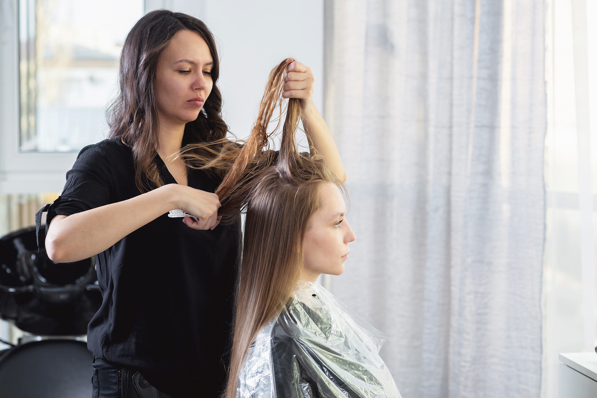 Close up of hairdressers hands drying long blond hair with blow dryer and round brush