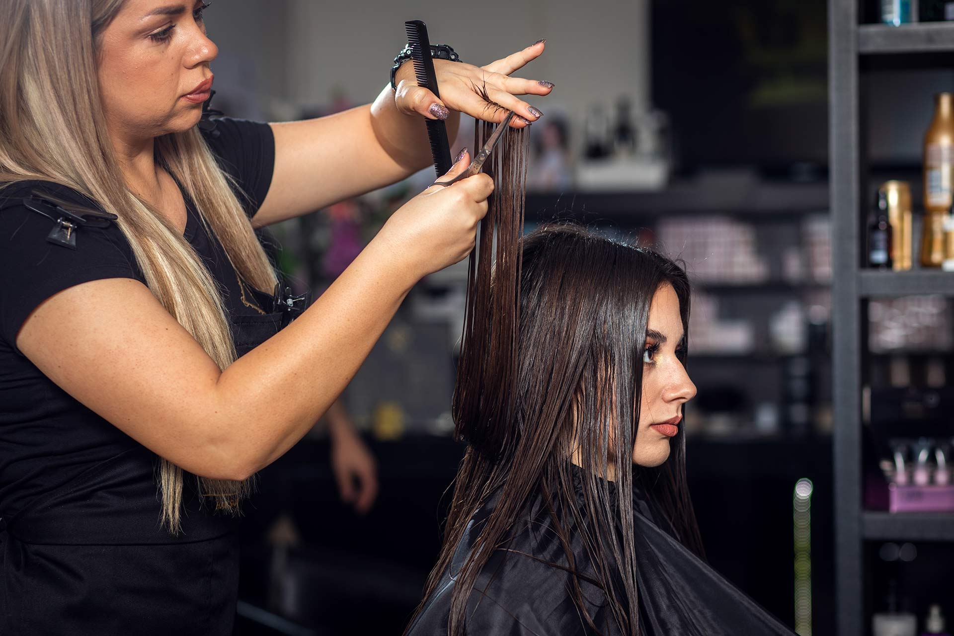 Female hairdresser makes hairstyle on young brunette woman in salon cutting hair with scissors.